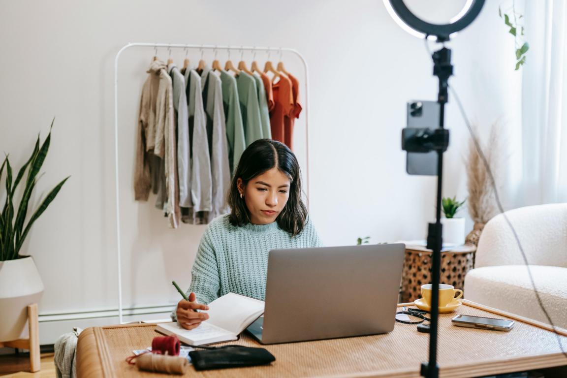Eine junge Frau sitzt an ihrem Schreibtisch und schreibt auf ihrem Blog und ihrem Laptop.