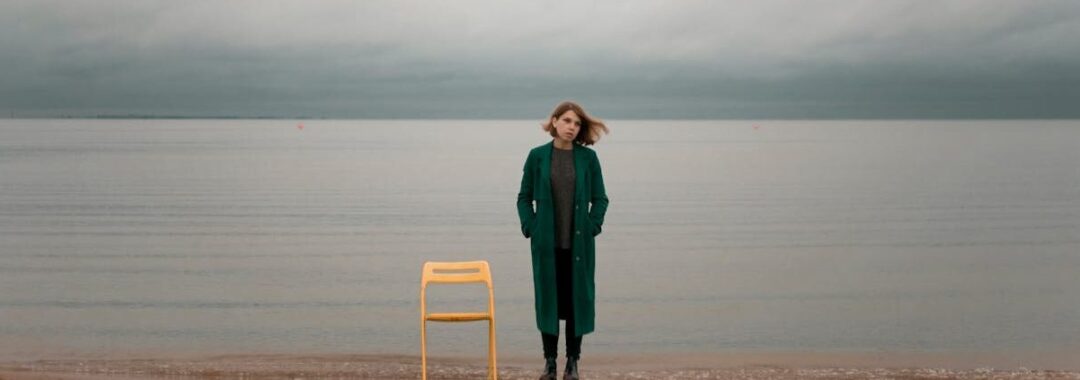 Nachdenkliche Frau neben leerem Stuhl am Strand – Metapher für warum sich mein Leben nicht verändert