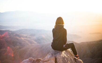 Frau sitzt auf einem Felsen und blickt in die Ferne – symbolisch für das Innehalten und Reflektieren