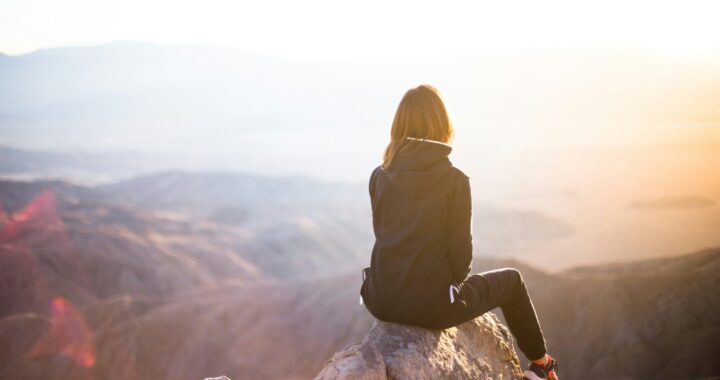 Frau sitzt auf einem Felsen und blickt in die Ferne – symbolisch für das Innehalten und Reflektieren