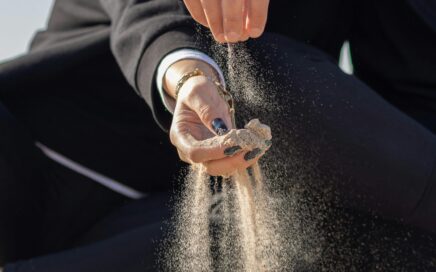Sand rinnt durch die Hände einer Frau am Strand – sinnbildlich für den Prozess des Loslassens