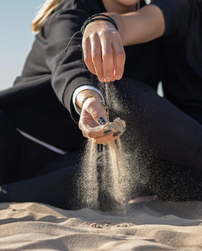 Sand rinnt durch die Hände einer Frau am Strand – sinnbildlich für den Prozess des Loslassens