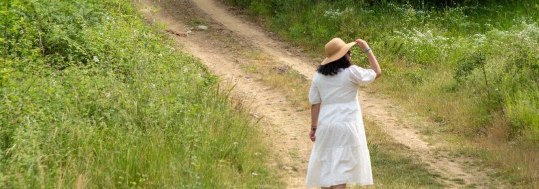 Kopf frei bekommen Eine Frau im weißen Kleid und einem eleganten Sonnenhut spaziert auf einem Feldweg, um ihre Gedanken zu ordnen, den Alltag hinter sich zu lassen und den Kopf komplett frei zu bekommen.